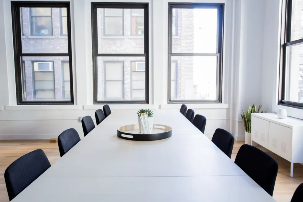 Φωτογραφία άδειας αίθουσας συνεδριάσεων με μακρύ λευκό τραπέζι και μαύρες καρέκλες δίπλα σε μεγάλα παράθυρα