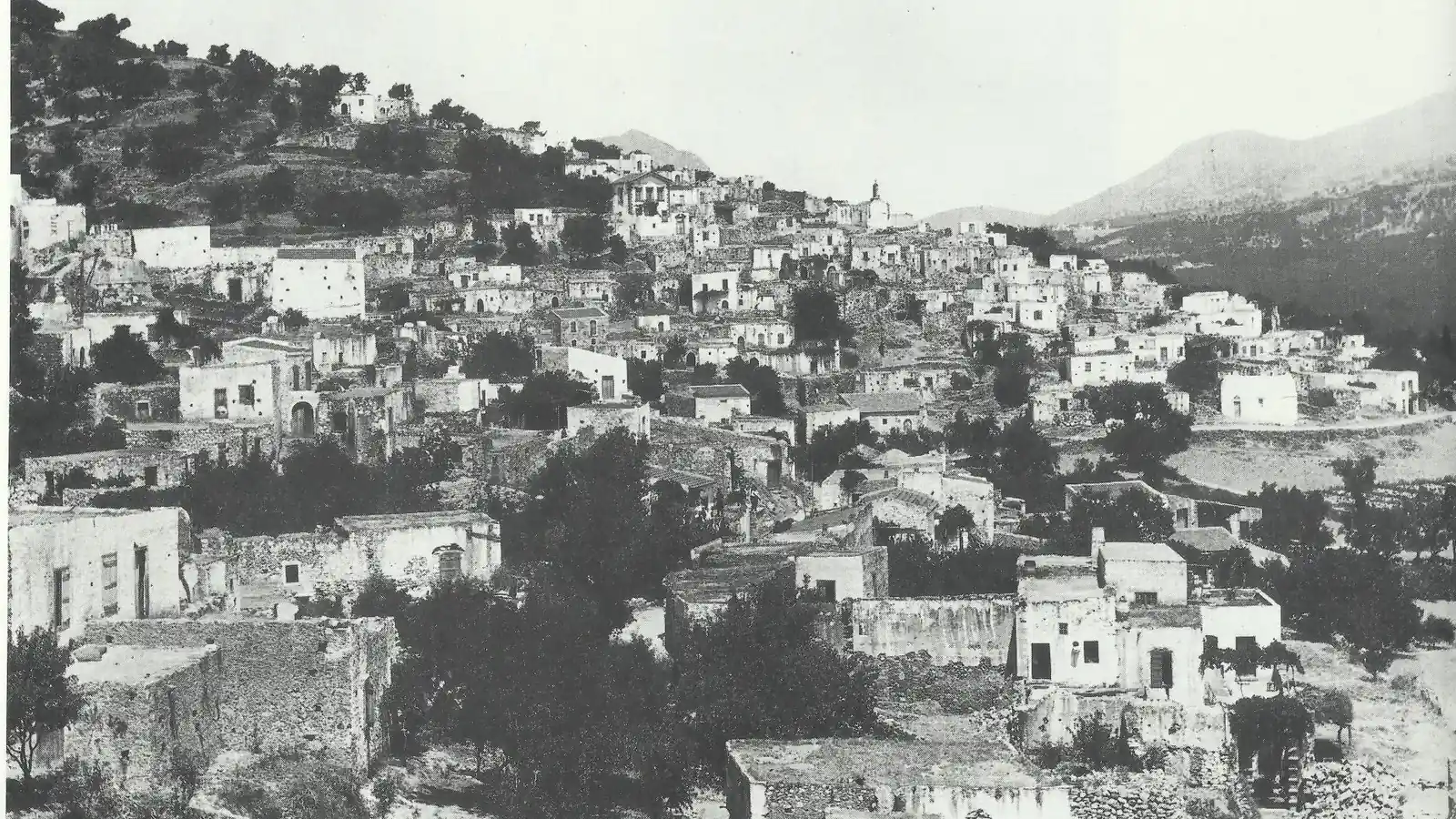 Ασπρόμαυρη φωτογραφία χωριού της Κρήτης με πέτρινα σπίτια σε πλαγιά, για τα ακίνητα στους μικρούς οικισμούς