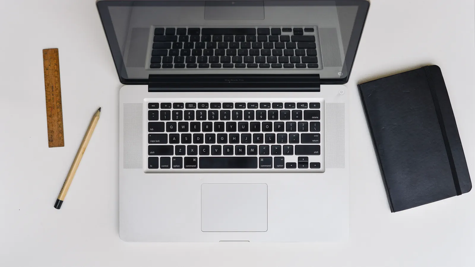 Φωτογραφία από ψηλά με laptop, μολύβι, χάρακα και μαύρο σημειωματάριο σε λευκό γραφείο