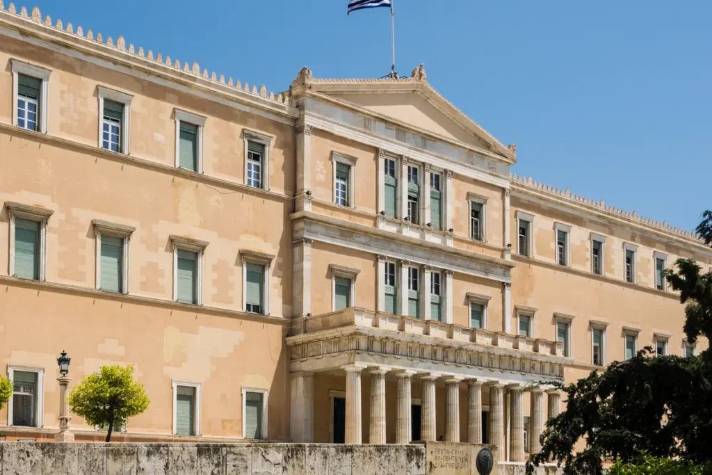 Φωτογραφία της πρόσοψης της Βουλής των Ελλήνων στην Αθήνα με τη σημαία στον ουρανό