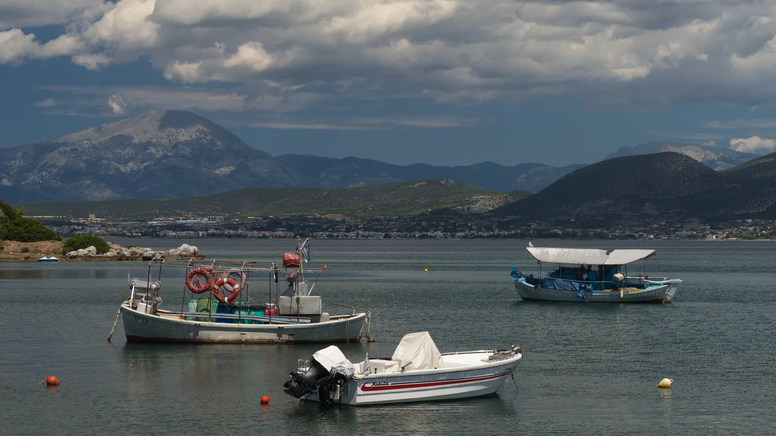 Φωτογραφία με ψαρόβαρκες αγκυροβολημένες σε ήρεμο κόλπο της Χαλκίδας, με βουνά και συννεφιά στο βάθος